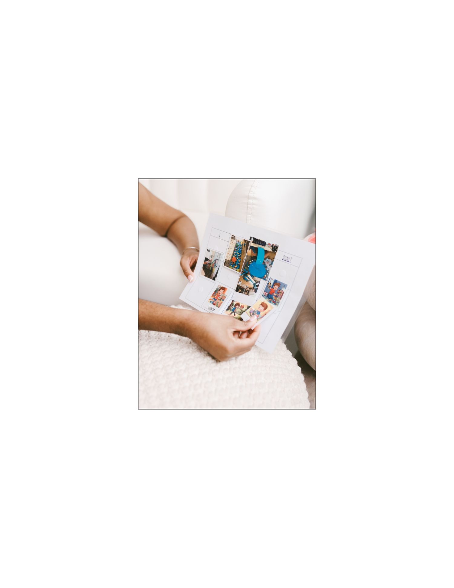 Person holding open a photo book filled with colorful pictures while sitting on a white textured chair.