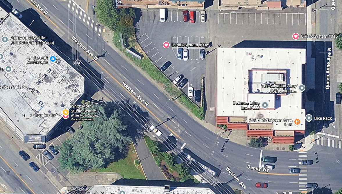 Aerial view of a busy urban intersection with roads, parking lots, and commercial buildings visible from above.