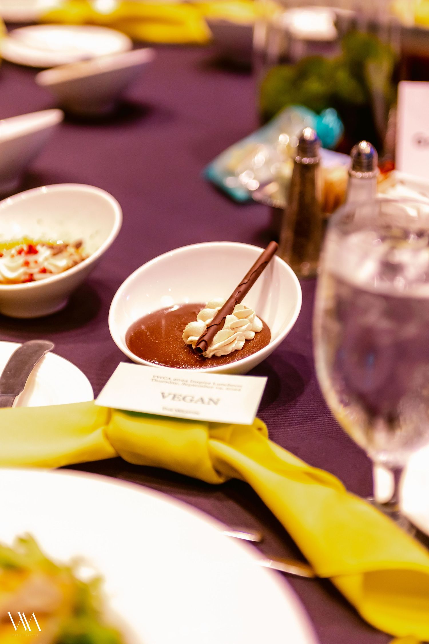 Elegant vegan dessert in white bowl with whipped cream on purple tablecloth at formal dining event.