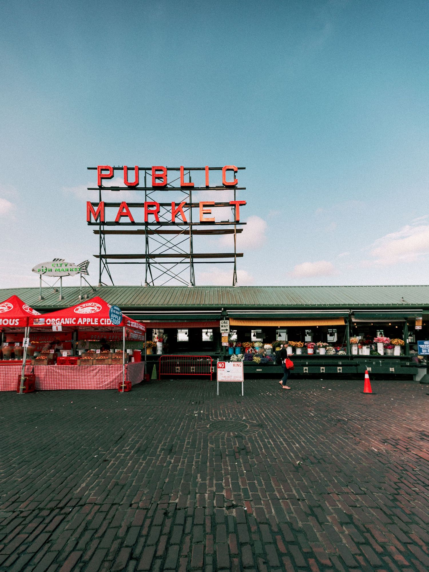 Pike Place Public Market in Seattle, WA, featuring iconic red neon sign, vendor stalls, and brick plaza under blue sky.