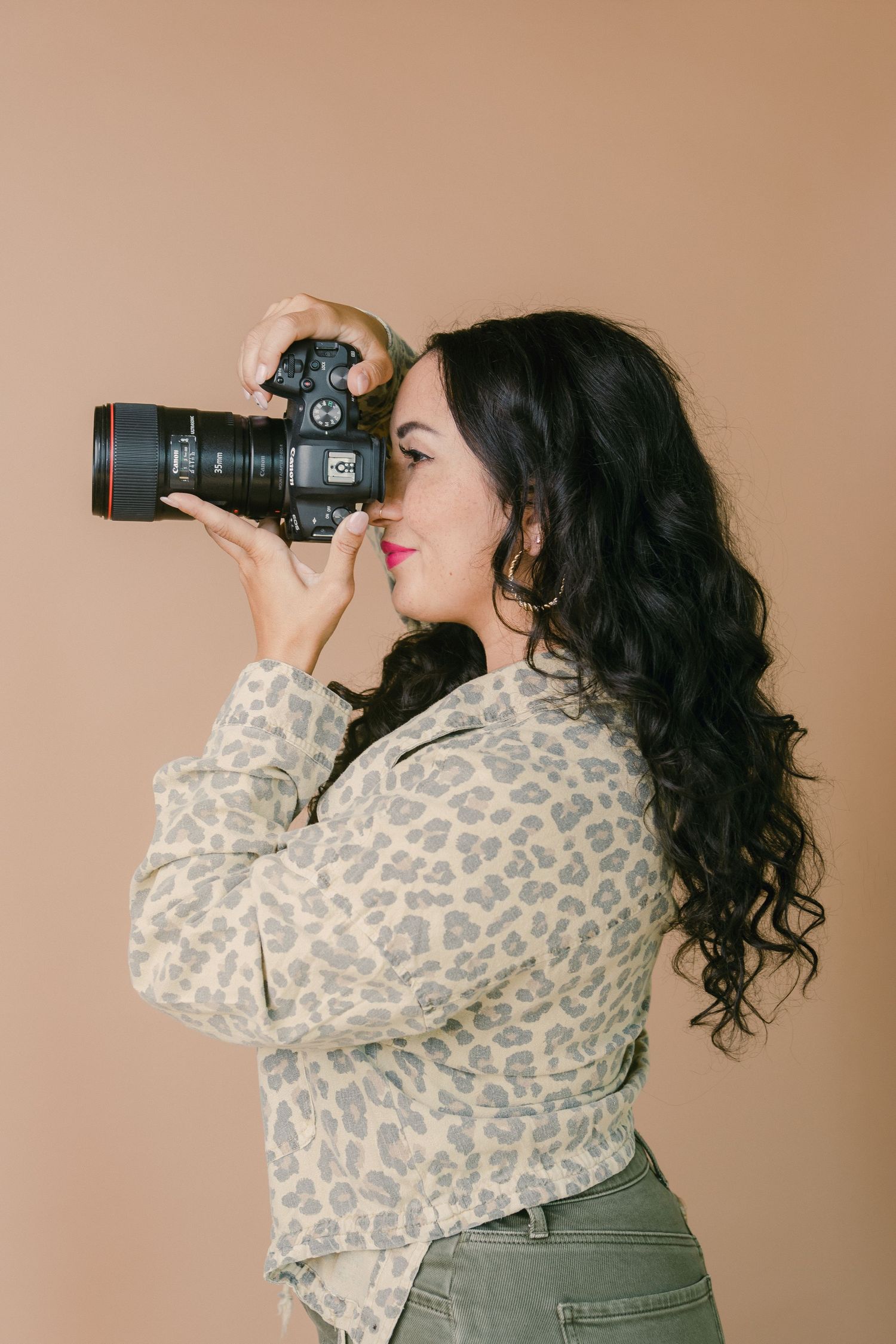 Woman in leopard print shirt photographing with a Canon DSLR camera against a beige background.
