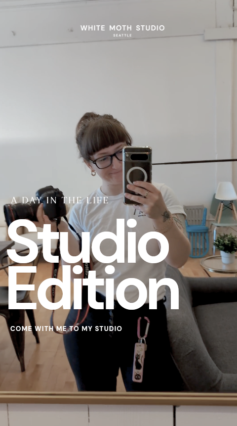 A photographer takes a mirror selfie in a bright Seattle studio, holding a camera, wearing glasses, for White Moth Studio.