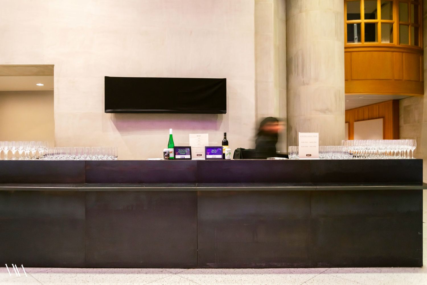 Modern bar counter with glassware, bottles, and a TV screen in an elegant venue interior.