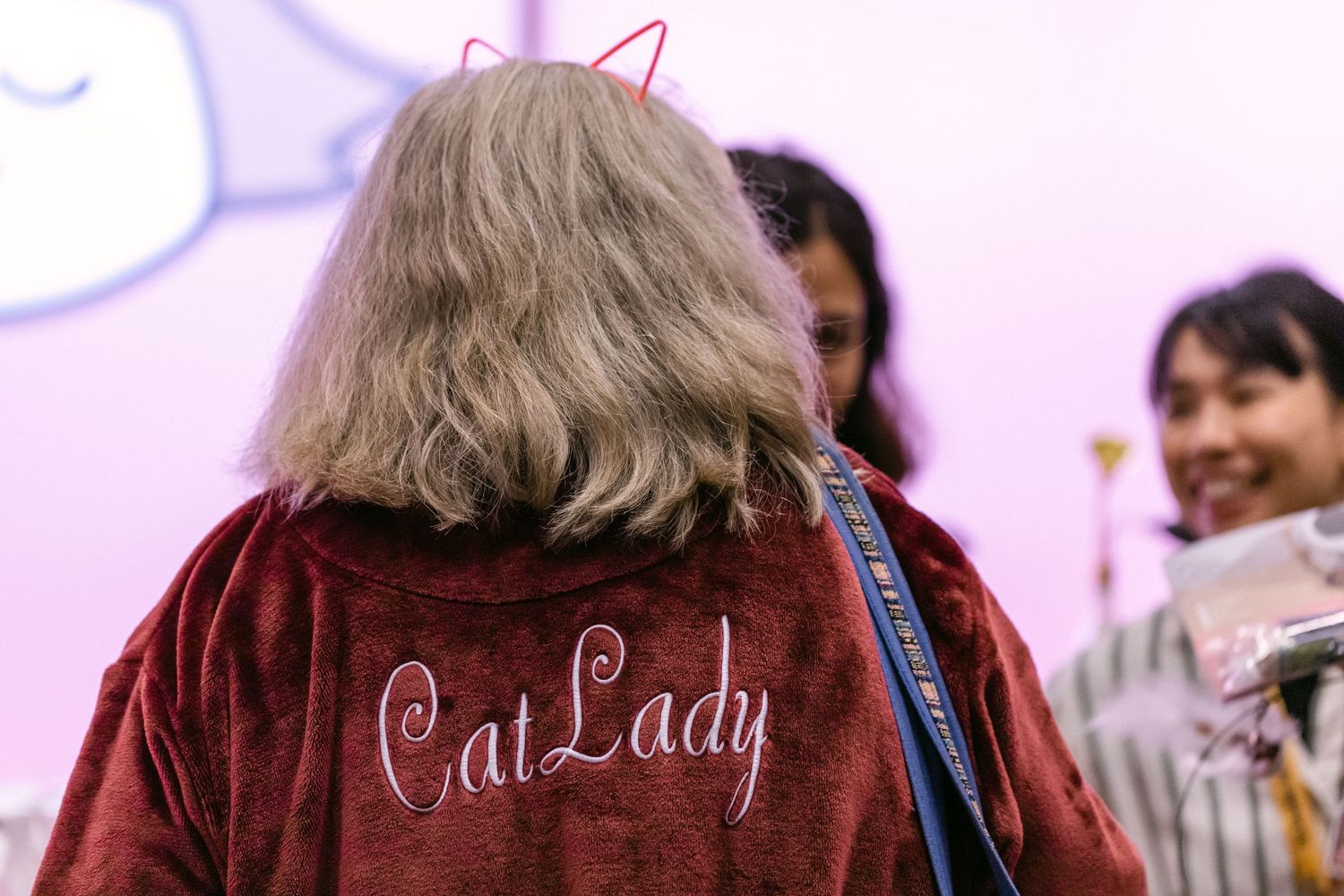 Woman wearing a red velvet Cat Lady jacket with cat ears headband at an indoor event.