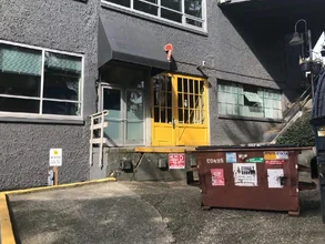 Yellow freight elevator on exterior of gray building beside a large red dumpster in an urban alley.