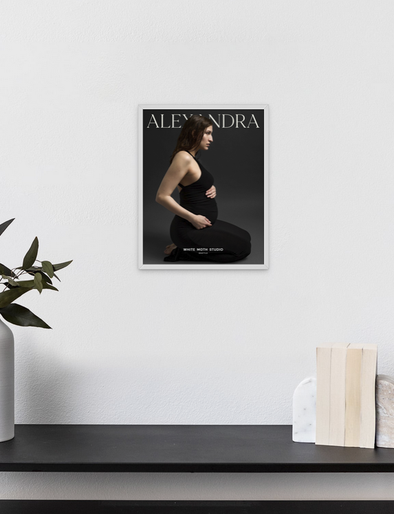 Framed maternity portrait print titled Alexandra displayed on a white wall above a dark shelf with decorative objects.