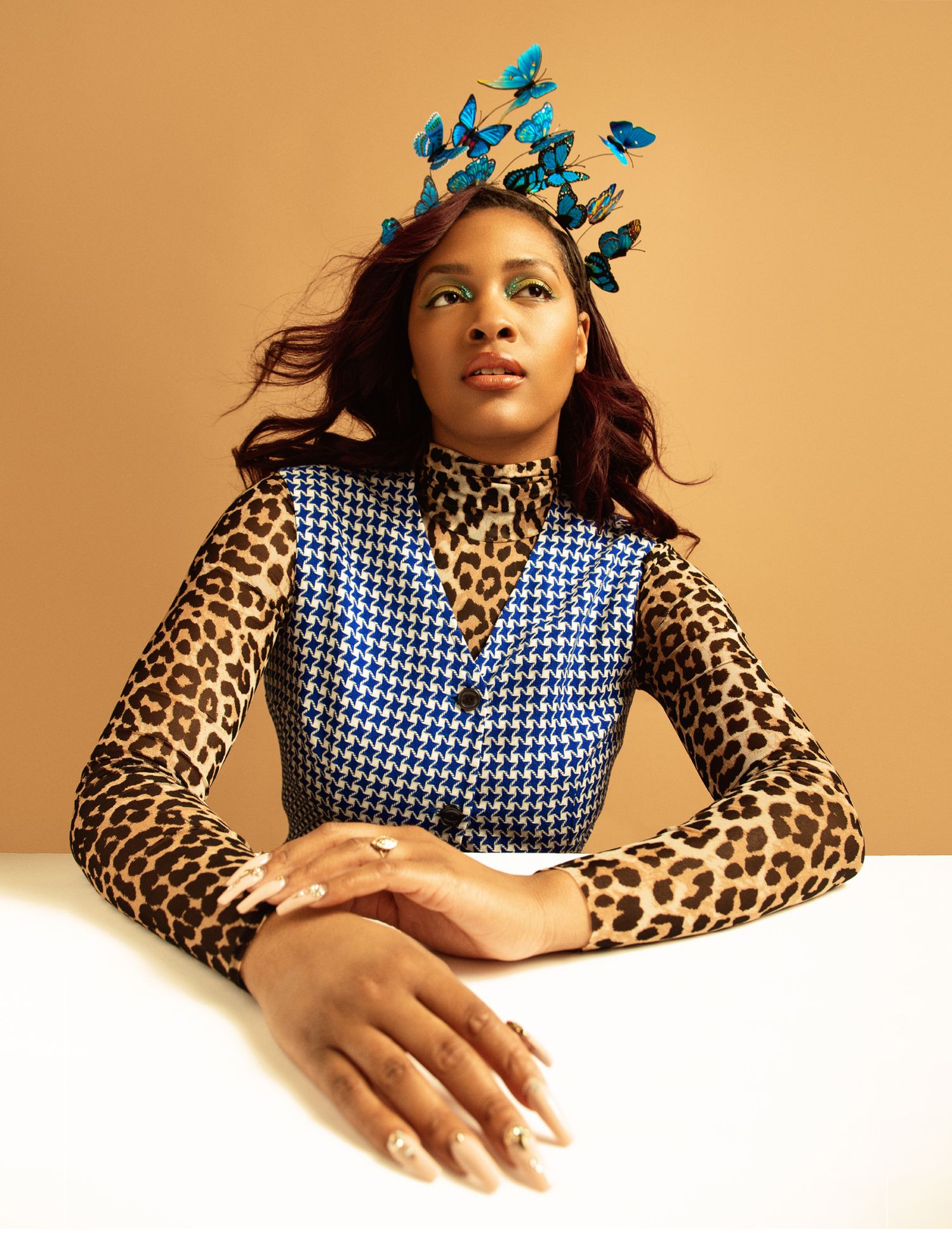 Fashion portrait of woman wearing blue houndstooth vest over leopard print top with blue butterfly crown headpiece.