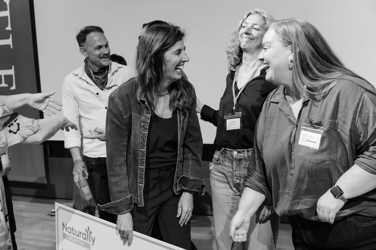 Group of women laughing together near Naturally branded sign at business conference.