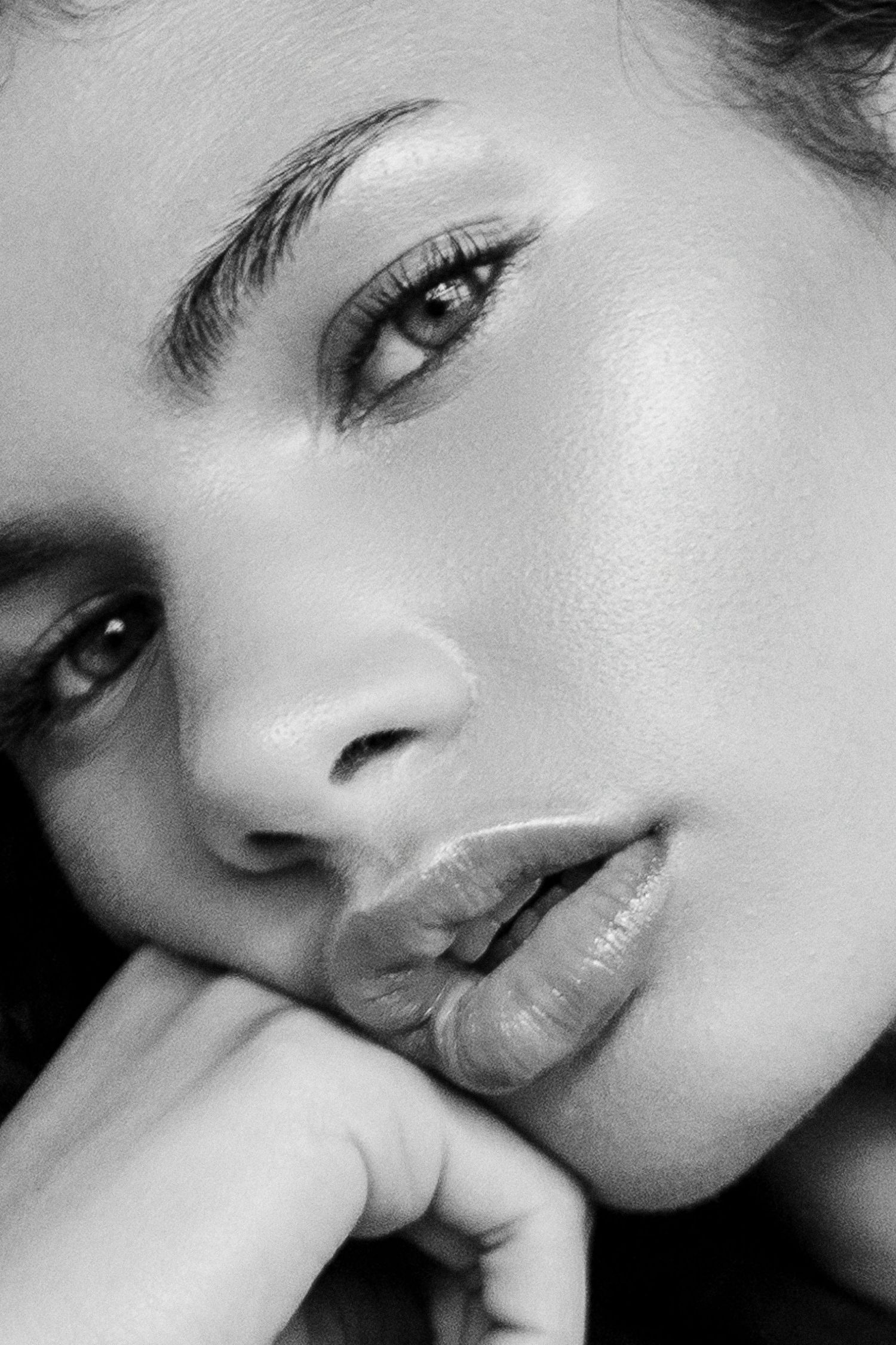 Black and white close-up portrait of a young woman with glossy lips and defined brows resting chin on hand.