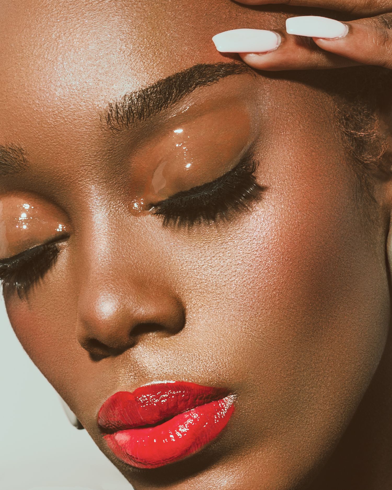 Close-up of a woman with glossy brown eyeshadow, bold red lips, and flawless dark skin, showcasing a stunning makeup look.