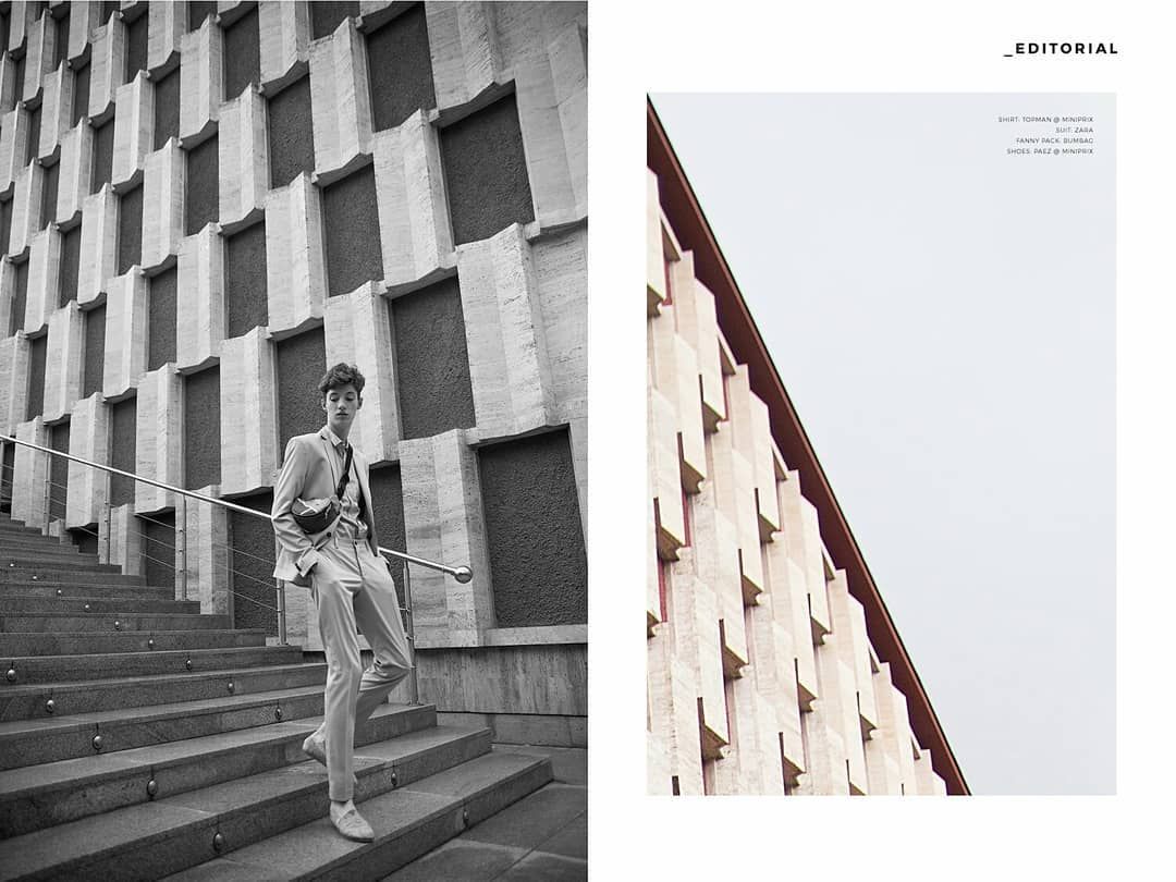 Black and white editorial fashion photo of male model on steps beside geometric building.