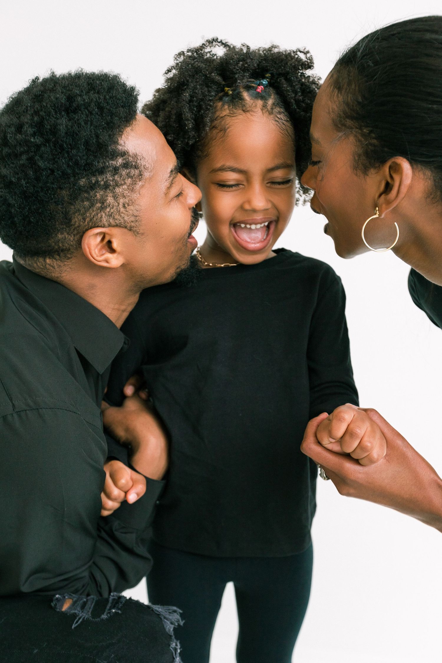 Happy African American family with parents leaning in toward laughing young daughter in matching black outfits.