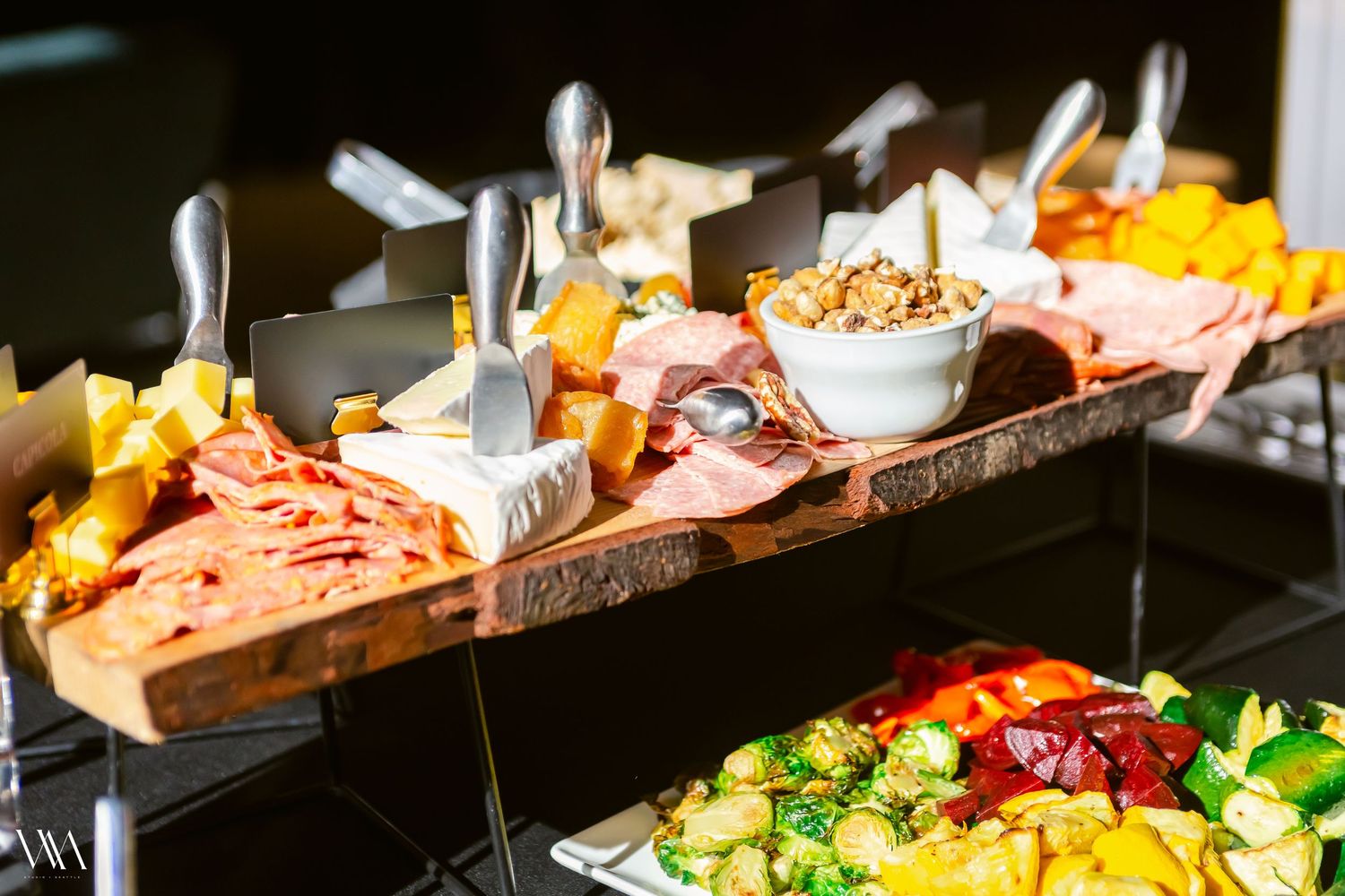 Elegant charcuterie board with cured meats, cheeses, and nuts displayed on rustic wood at a catered event.