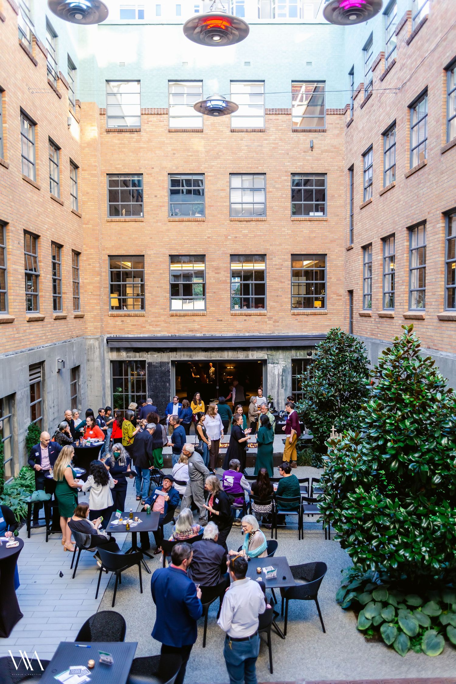 Aerial view of a corporate networking event in a brick courtyard with attendees mingling at outdoor tables.