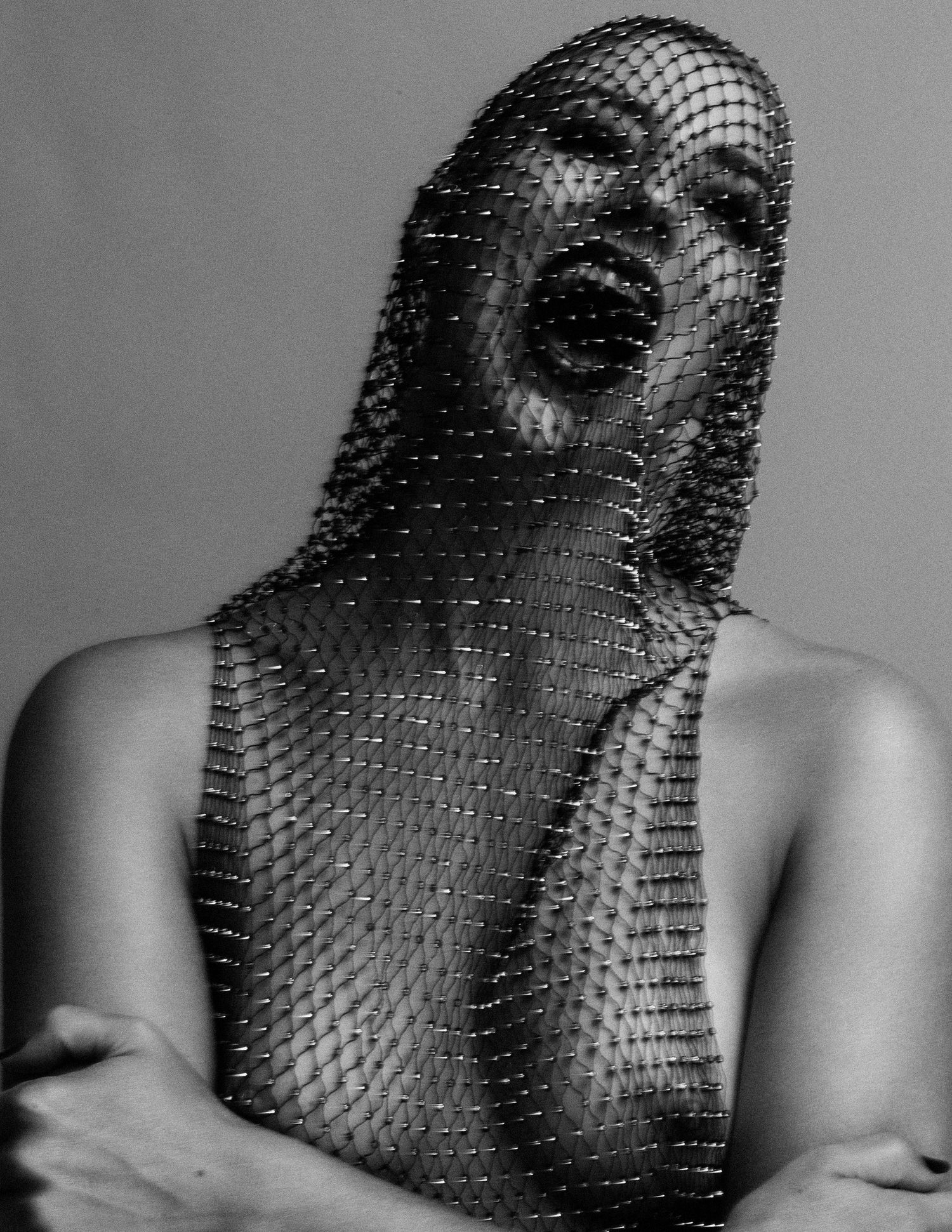 Black and white fashion photo of a model draped in mesh net fabric covering face and body in dramatic pose.