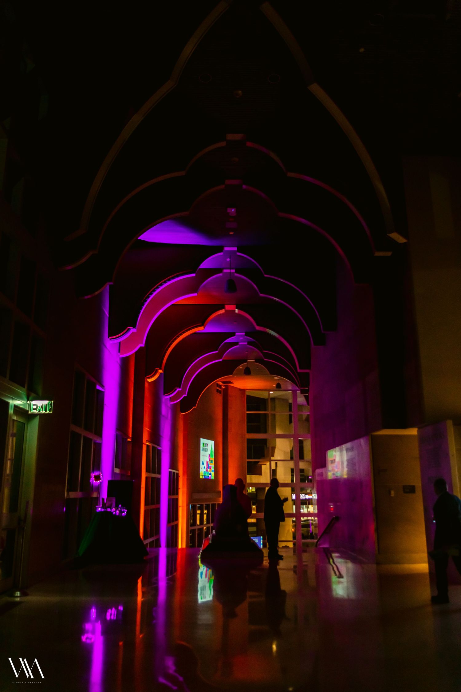 Dramatic event venue corridor with arched ceilings illuminated by vibrant purple and orange uplighting at night.