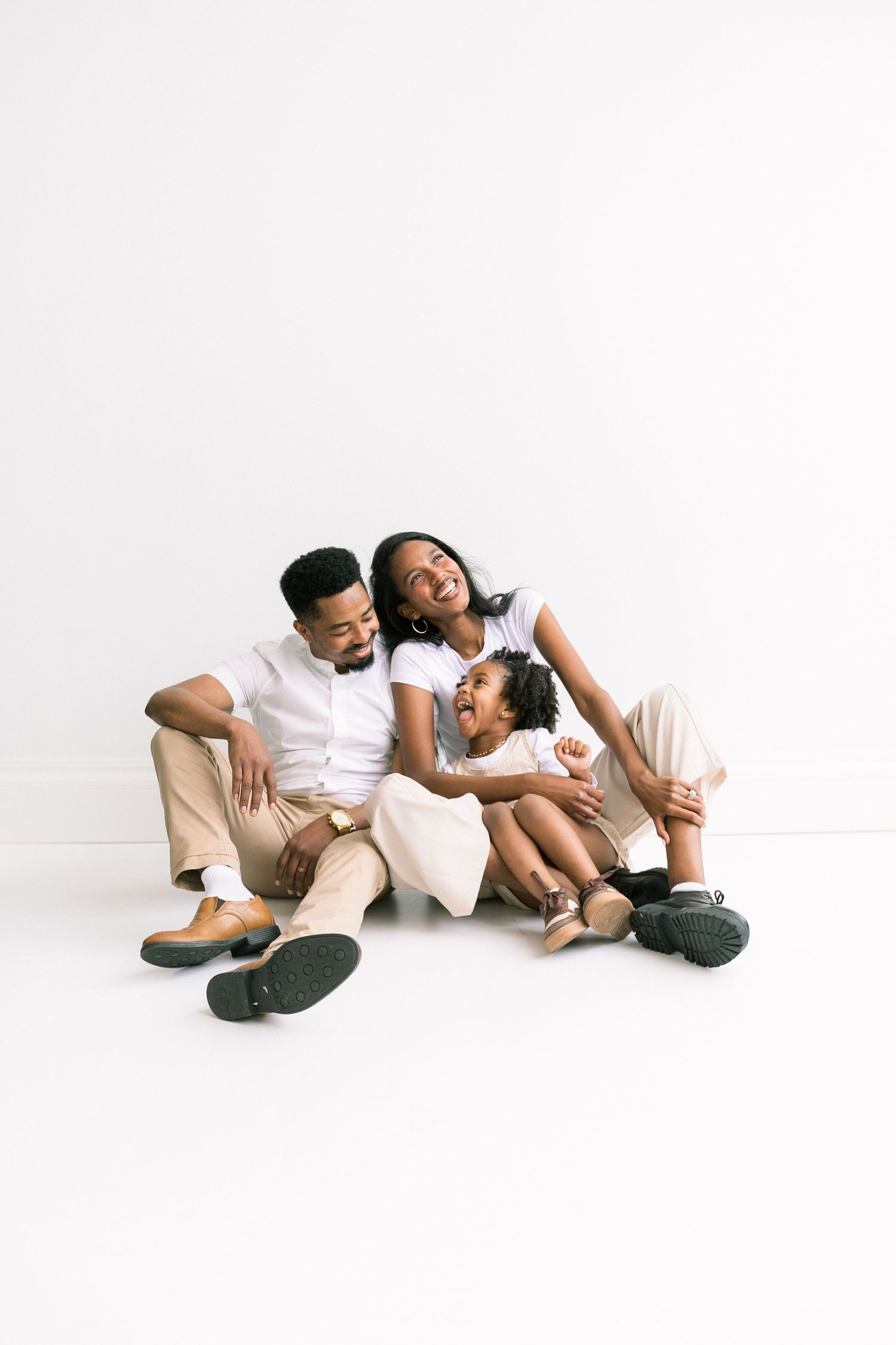 Happy family with young daughter sitting together laughing on white studio floor.