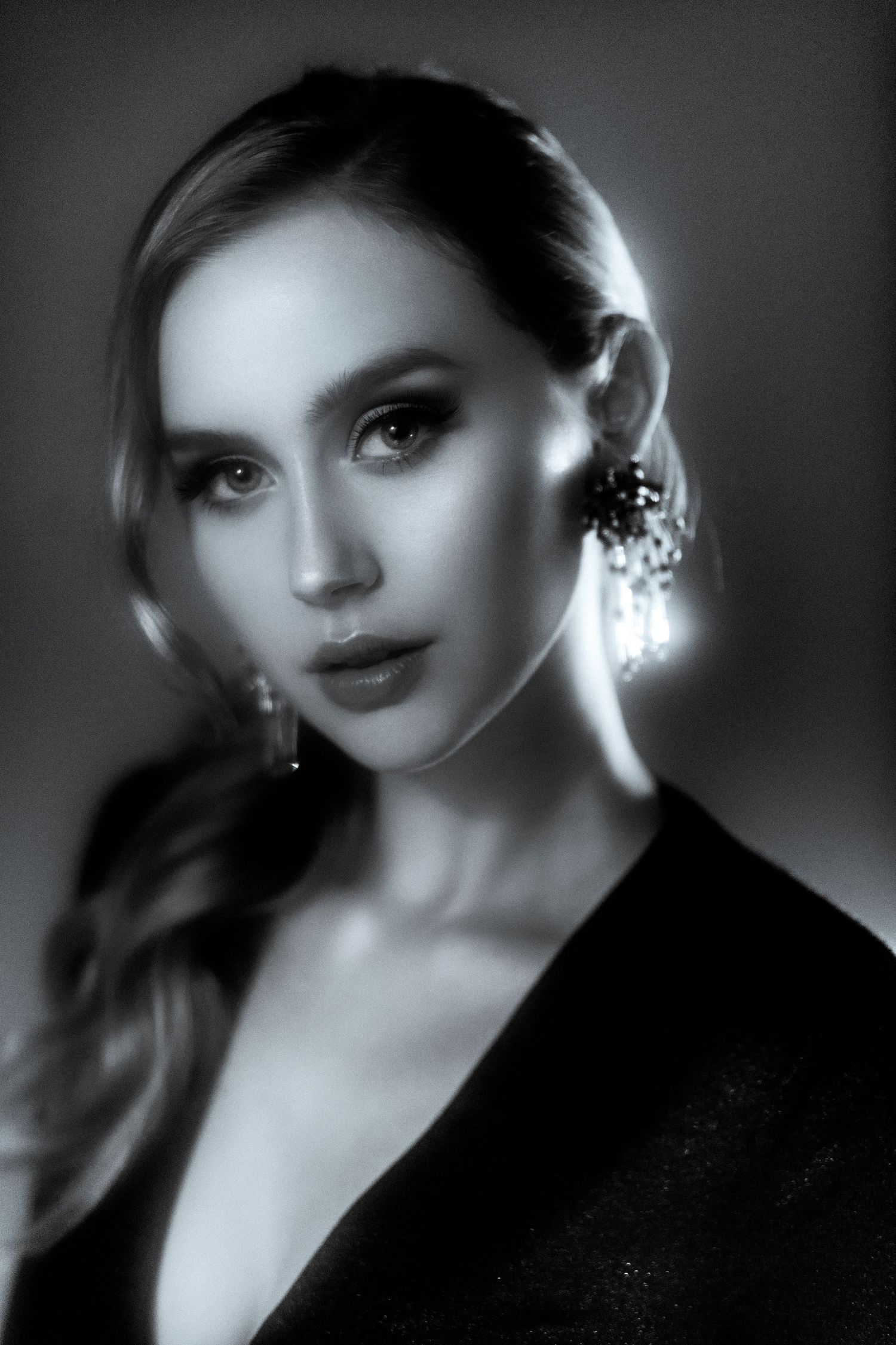 Black and white portrait of an elegant woman with dramatic earrings and smoky eye makeup in a dark blazer.