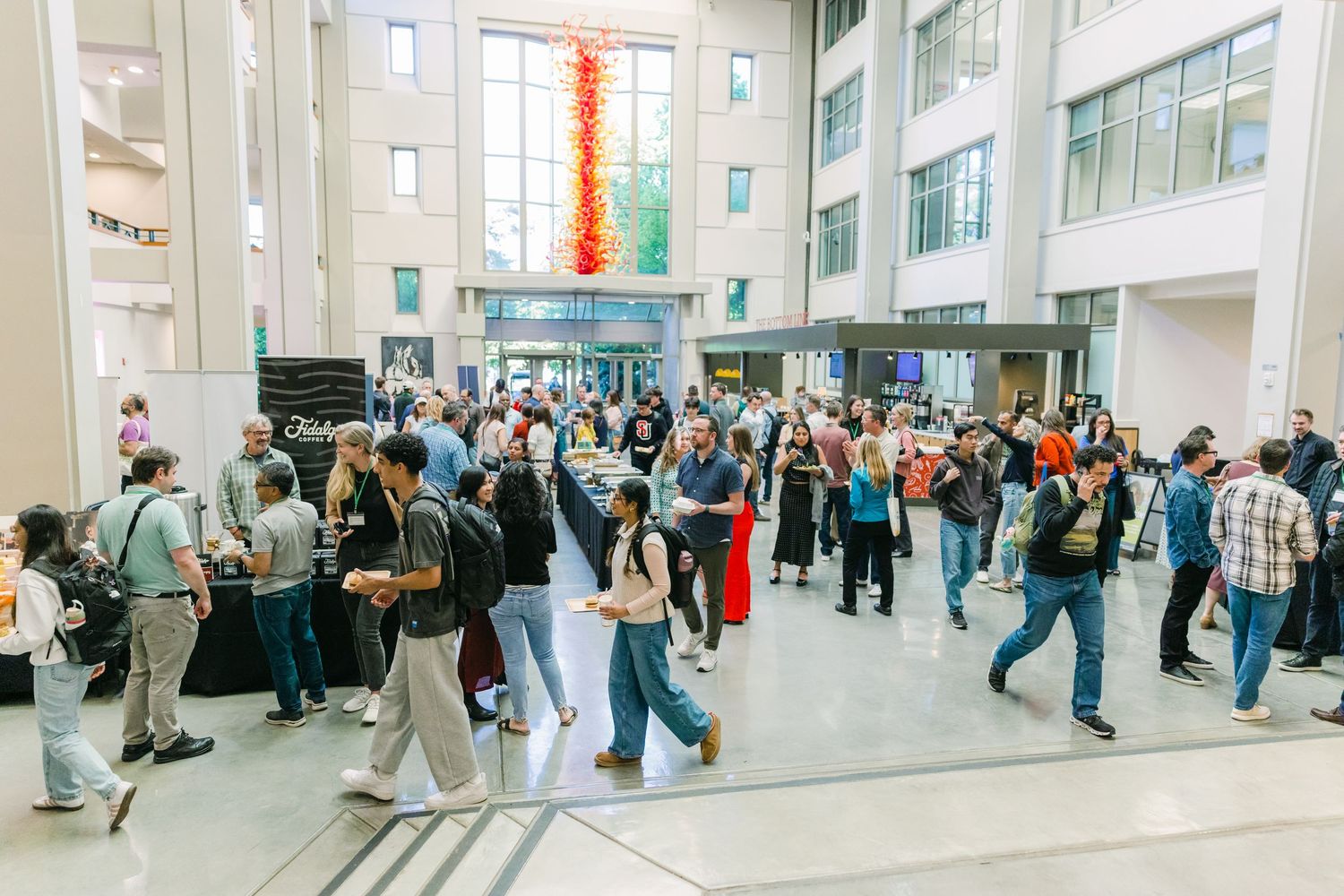 Large crowd gathers in a bright modern atrium lobby during a bustling indoor community event.