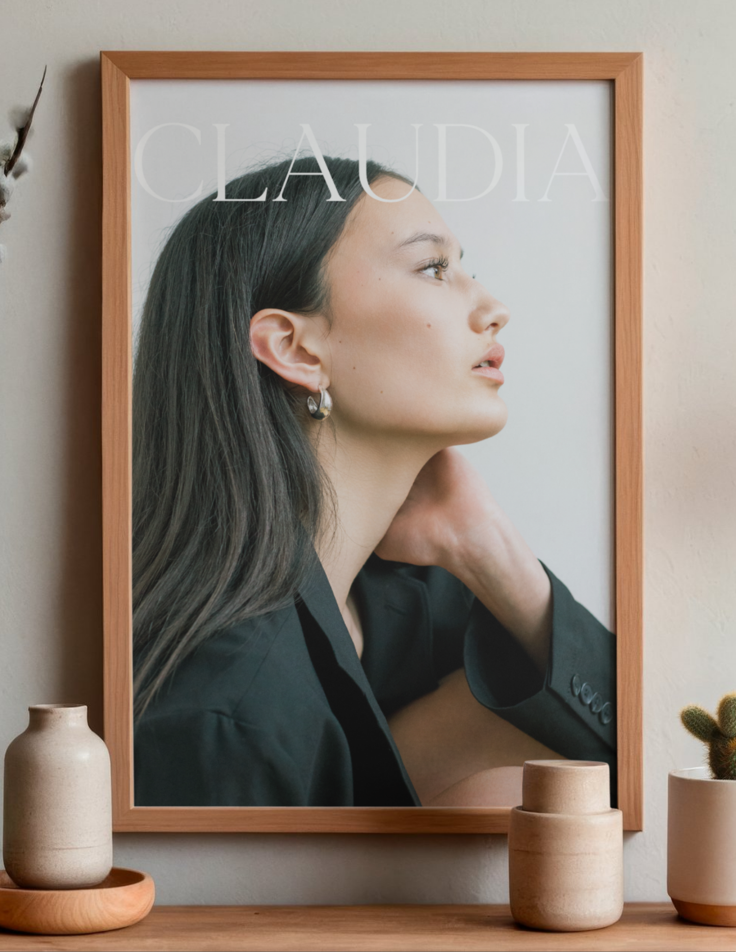A young woman in a dark blazer poses elegantly in a wooden-framed portrait poster titled Claudia, displayed on a shelf.