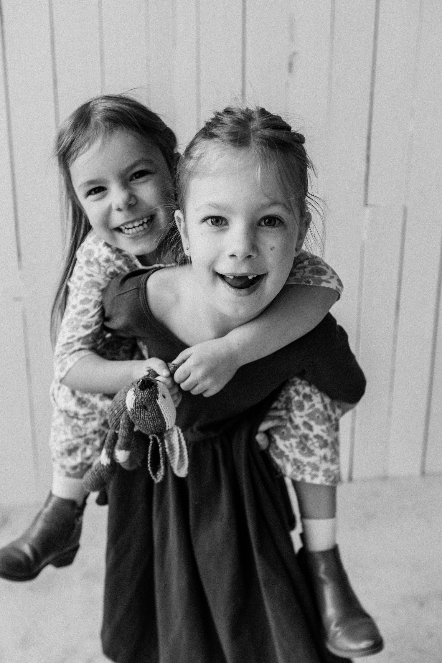 Two joyful young sisters hugging and laughing together in a playful black and white portrait photo.