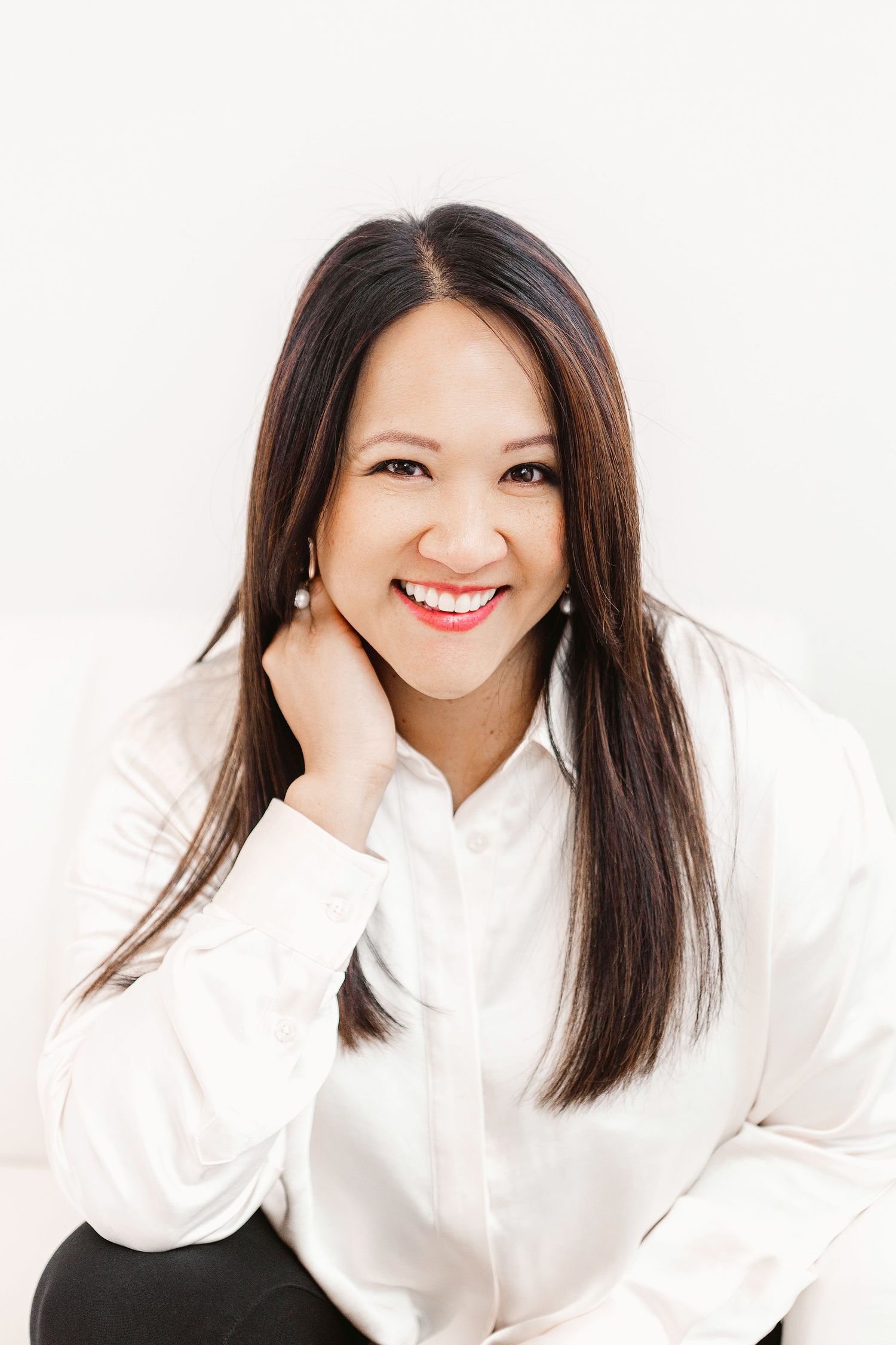 Smiling Asian woman with long dark hair wearing a white button-up shirt, posing casually against a white background.