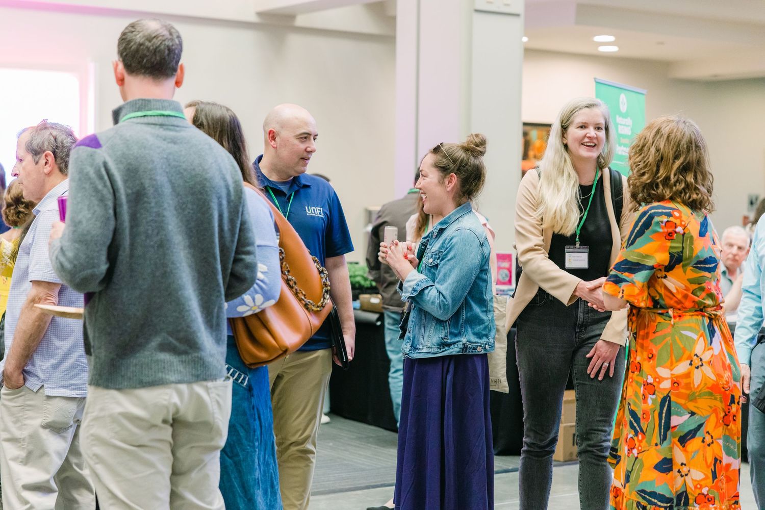 Professionals networking in conference hall wearing lanyards at industry gathering event.