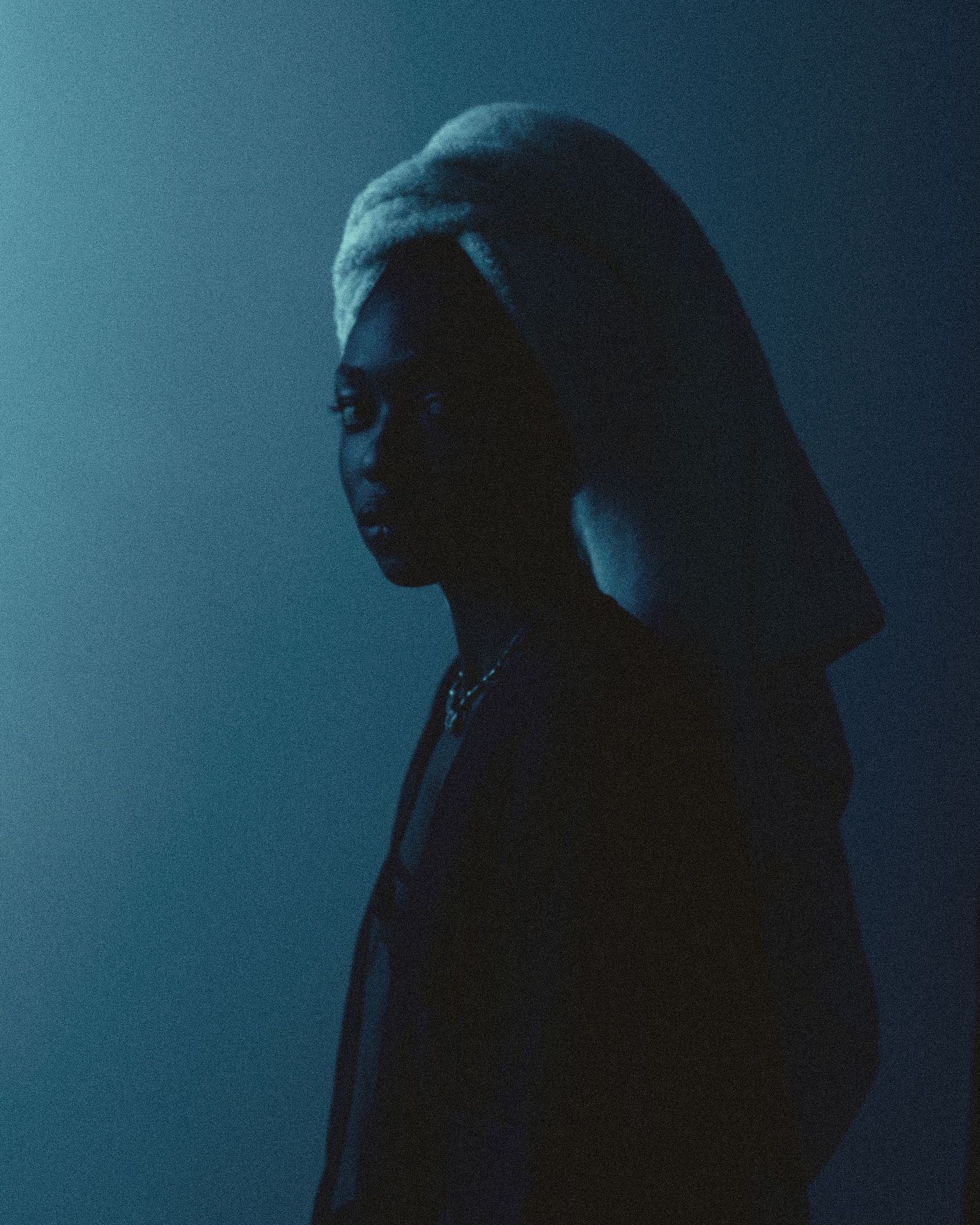 A person in a dark hoodie stands in dramatic blue-toned lighting, creating a moody silhouette portrait.