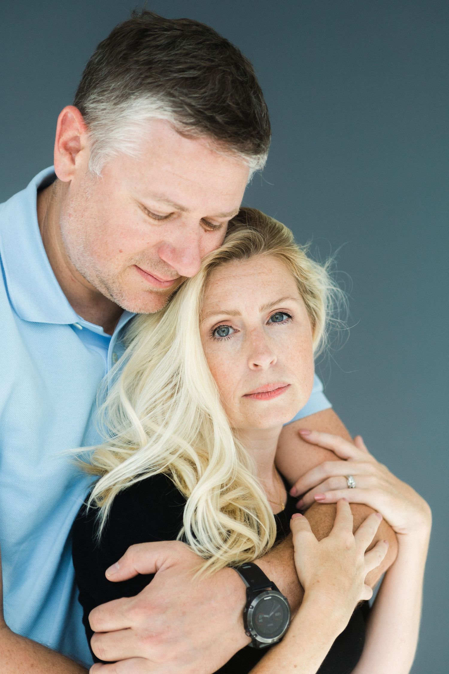 A mature couple shares a tender embrace, the man resting his head on the blond womans shoulder.