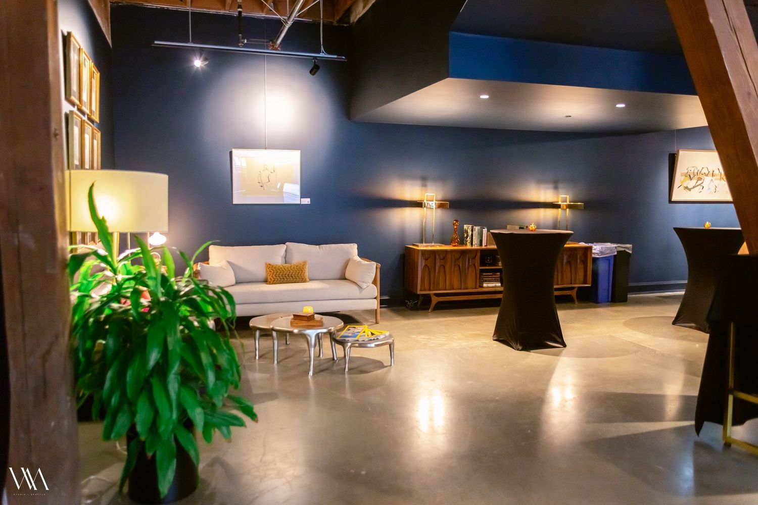 Modern event venue with blue walls, concrete floors, white sofa, and elegant furnishings perfect for upscale gatherings.