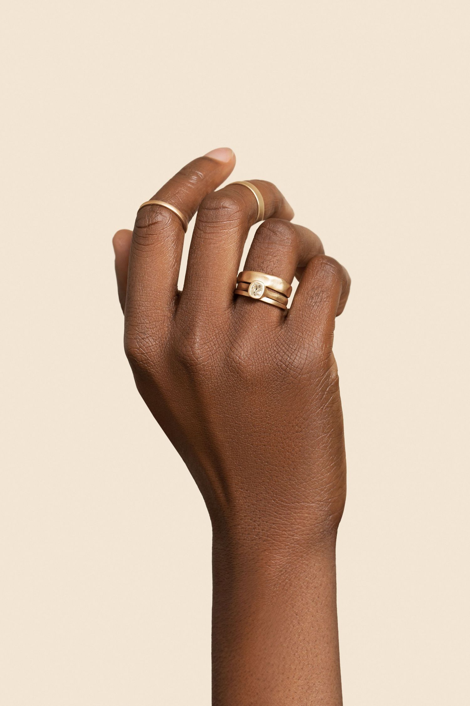 A dark-skinned hand elegantly posed wearing stacked gold rings including a wide band with diamond accent.