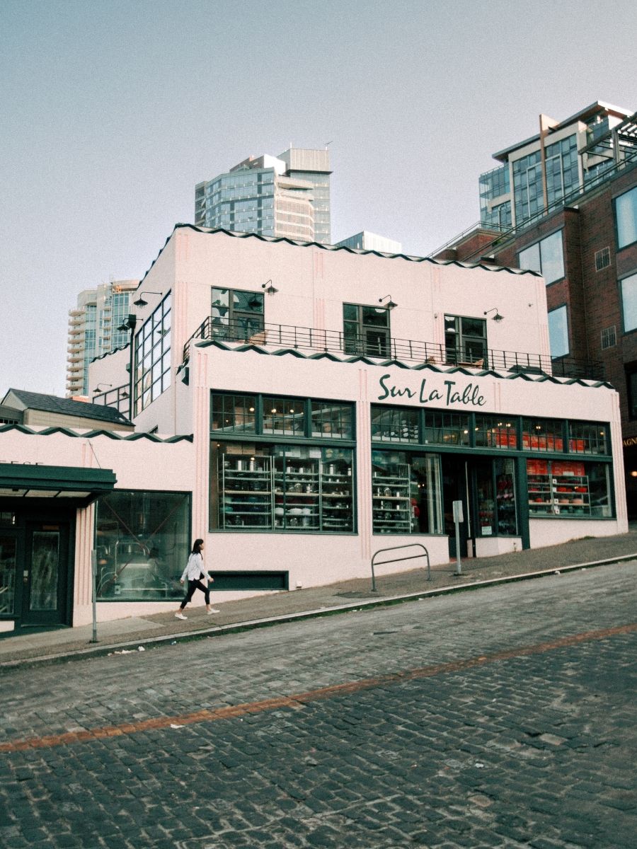 Sur La Table kitchen store exterior with pink facade and large display windows on a cobblestone street.