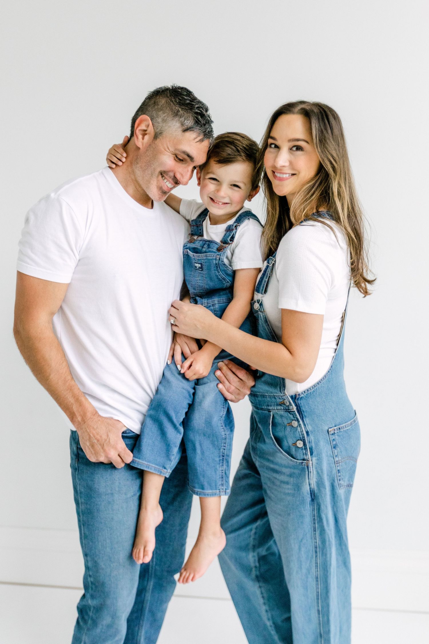 A happy family of three wearing matching white tees and denim, posing together against a white background.