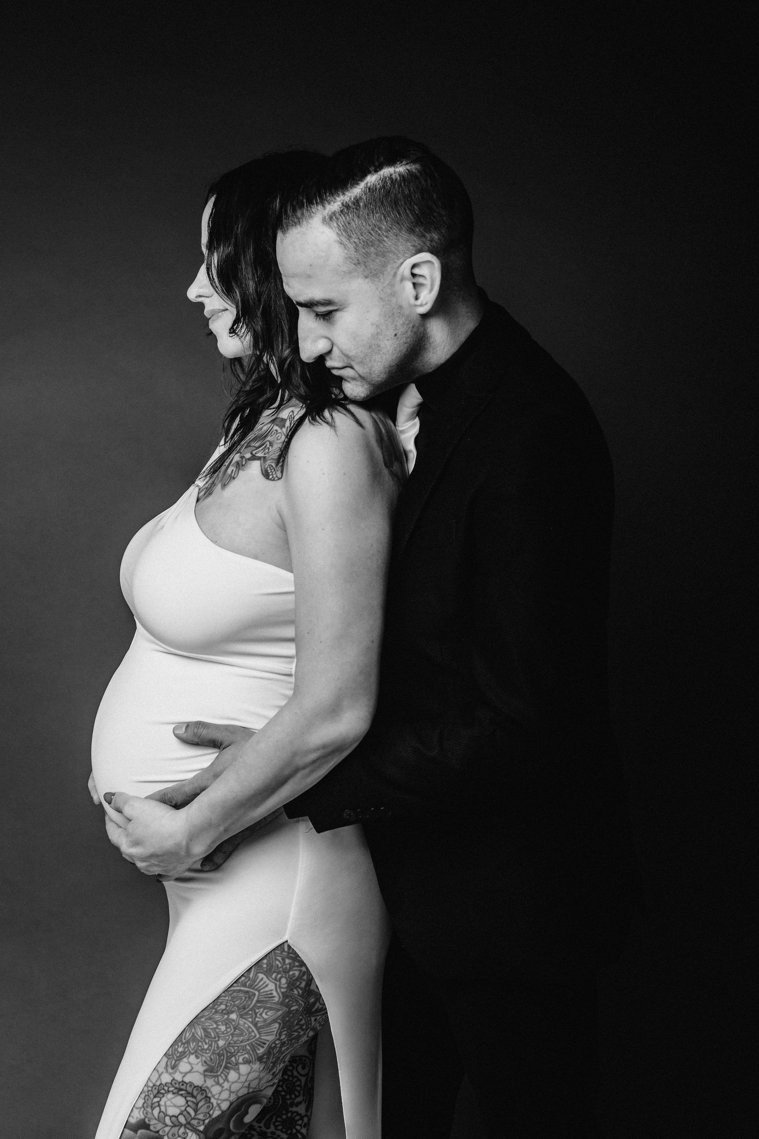 Black and white photo of couple embracing, man kissing pregnant woman's head.