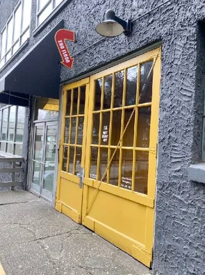 Yellow double doors on a dark textured building exterior with a red arrow sign and wall-mounted light fixture.
