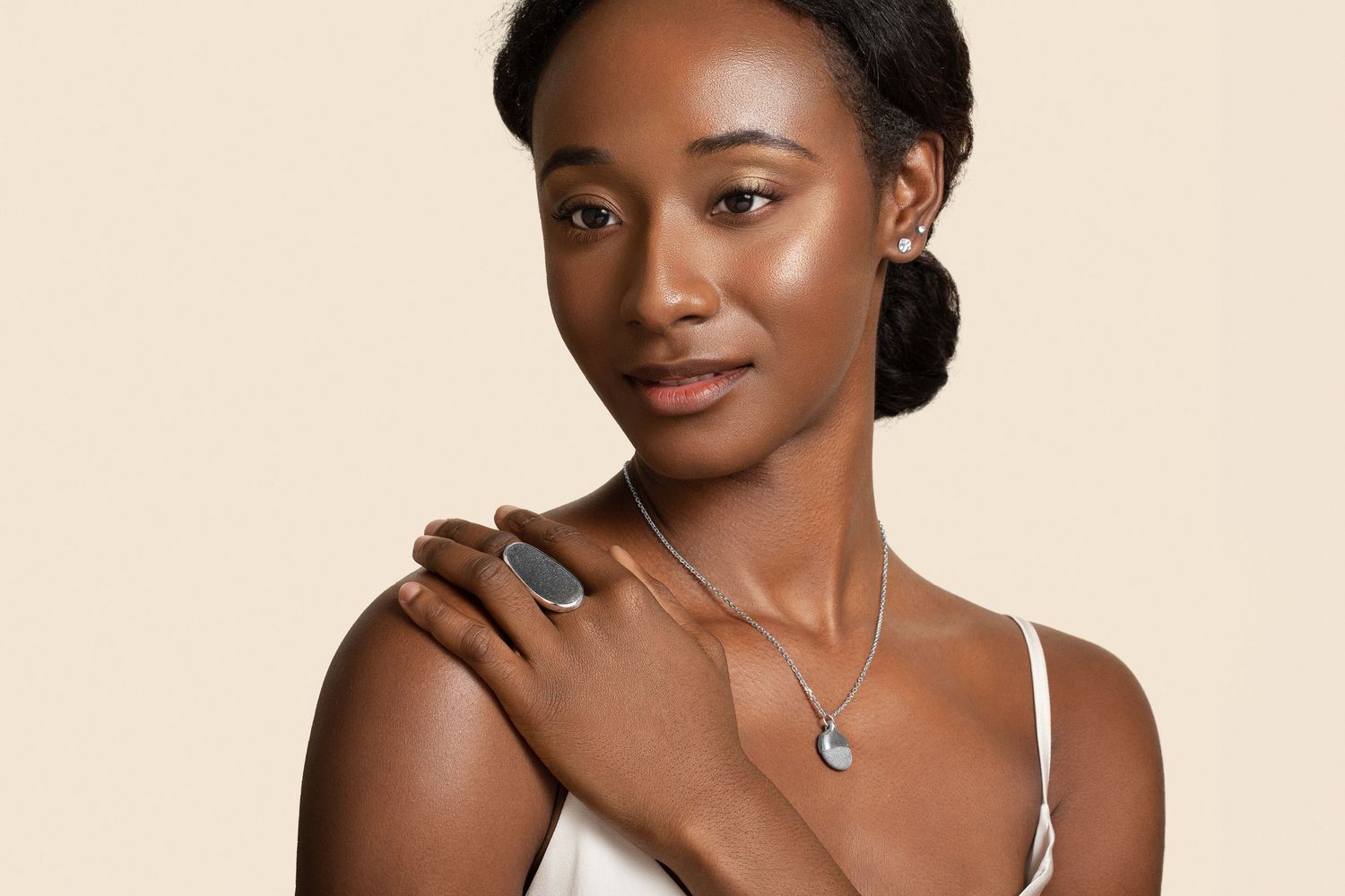 Woman wearing silver jewelry including a ring, necklace, and earrings against a beige background.