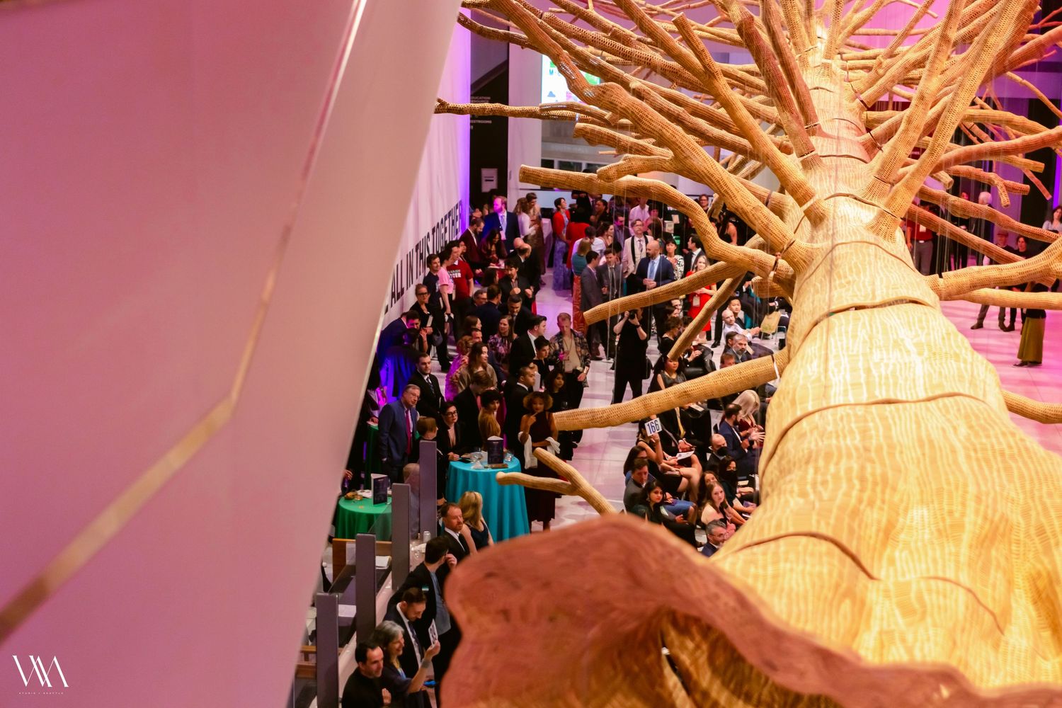 Aerial view of a large indoor event with crowds mingling around a large decorative tree sculpture.