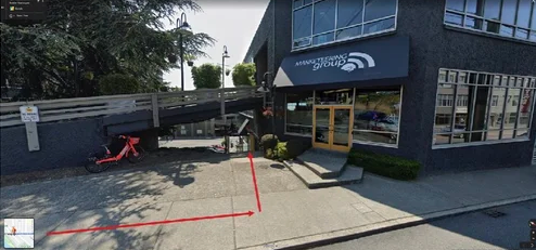 Street view of a modern commercial building with large windows and a blue storefront sign, featuring a marked parking area.