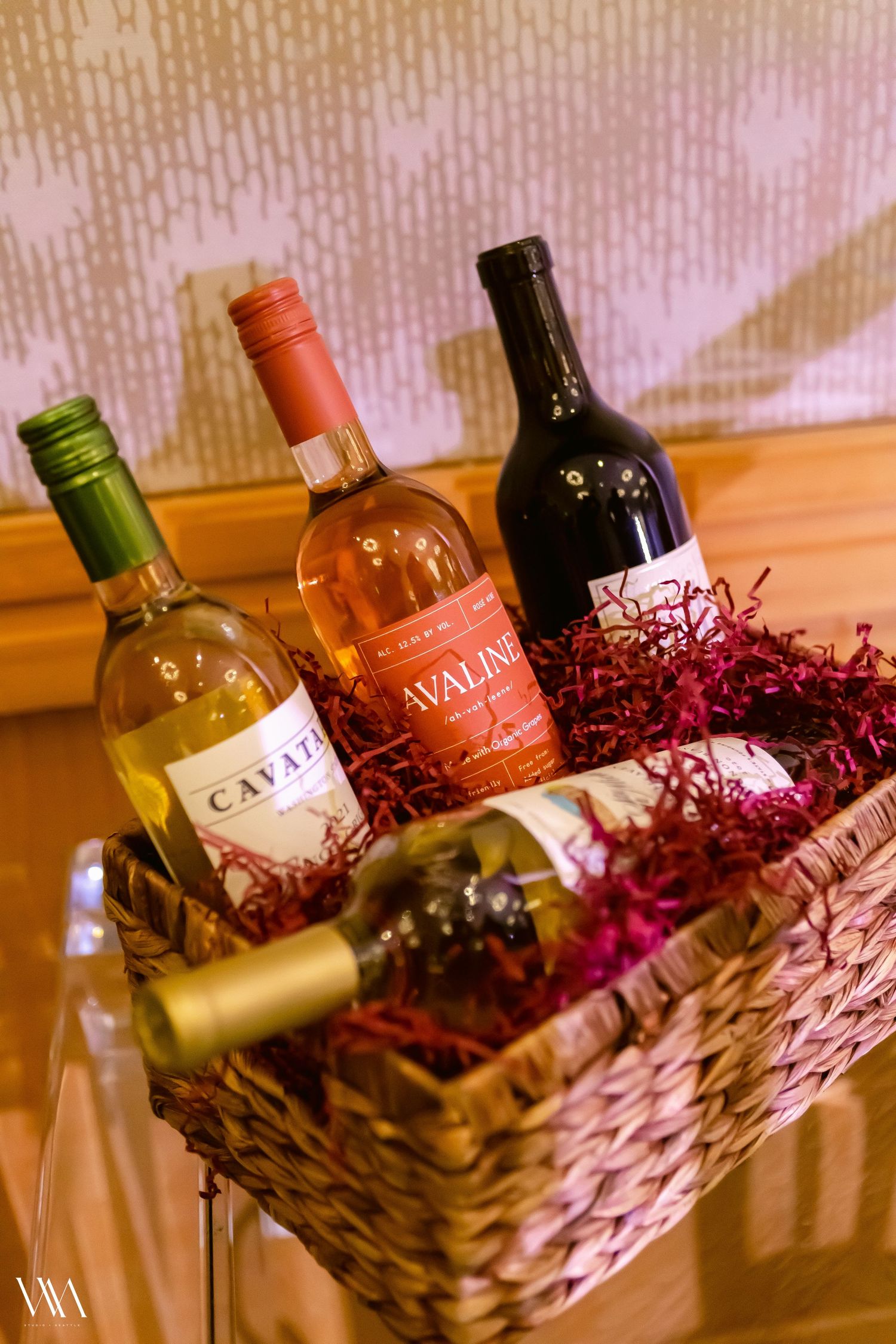 Wicker gift basket filled with red shredded paper and four Cavata and Cavalino wine bottles for a raffle prize.