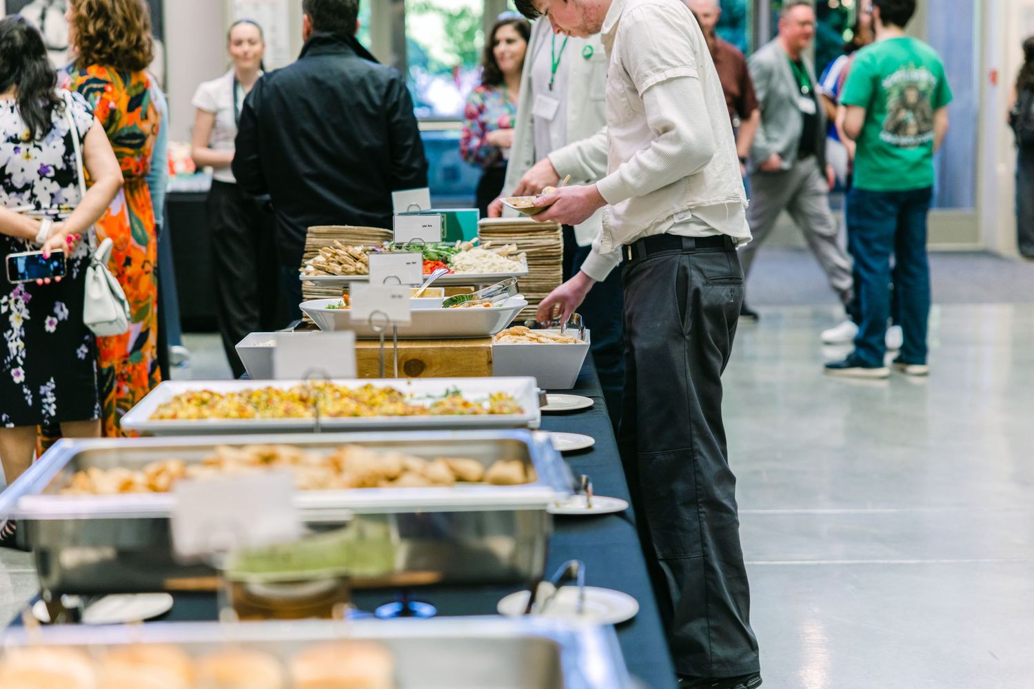 Guests serving themselves at a buffet table with chafing dishes at a catered corporate event.