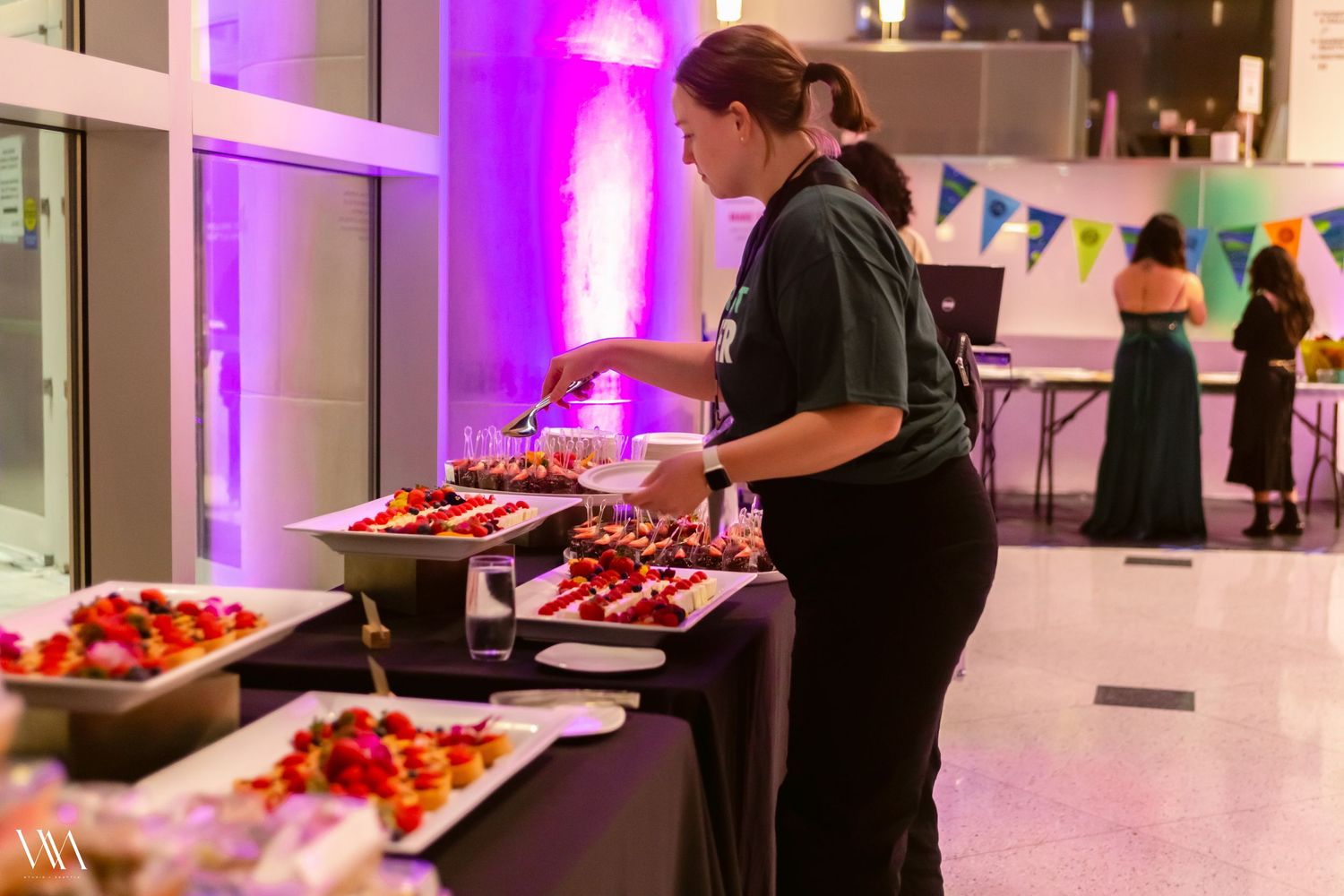 Catering staff member serving fresh fruit appetizers at an elegant indoor event with purple lighting.