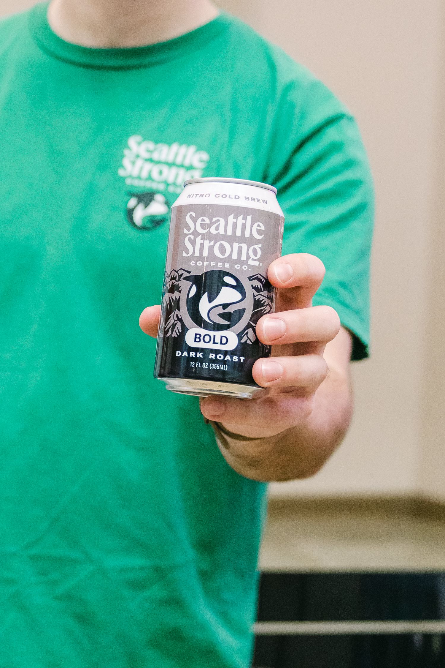 Person in green Seattle Strong t-shirt holding a Bold Dark Roast Nitro Cold Brew coffee can.