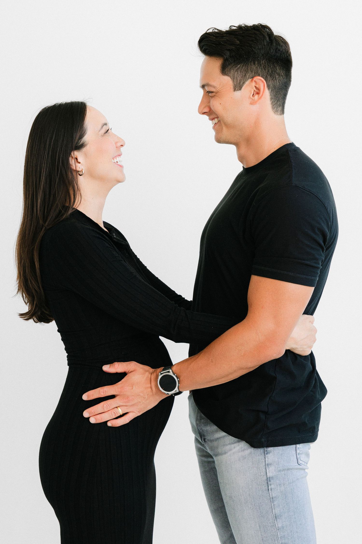 Happy couple in black outfits embracing and smiling at each other against white background.