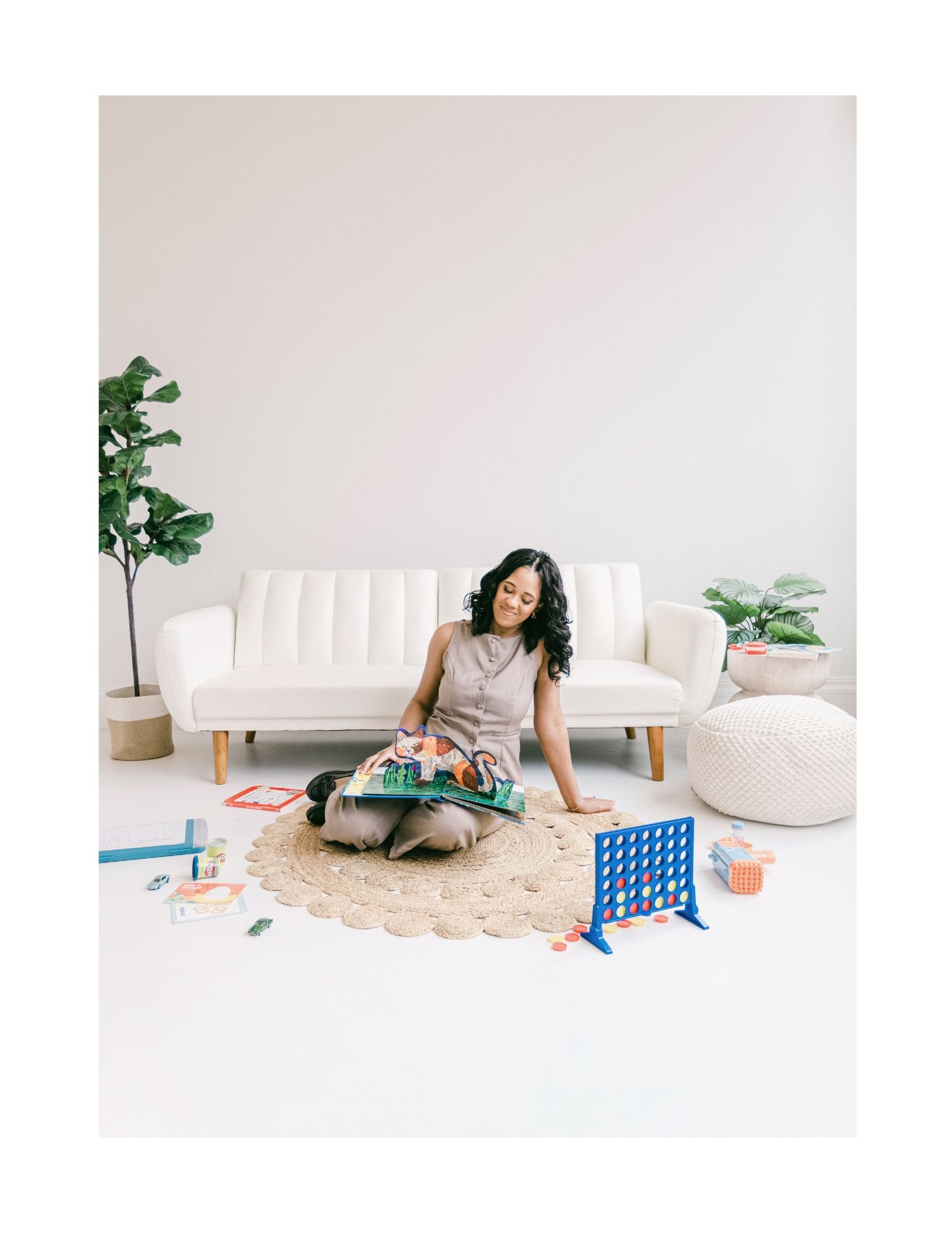 Woman sitting cross-legged on round rug with board games in bright minimalist living room with white sofa.