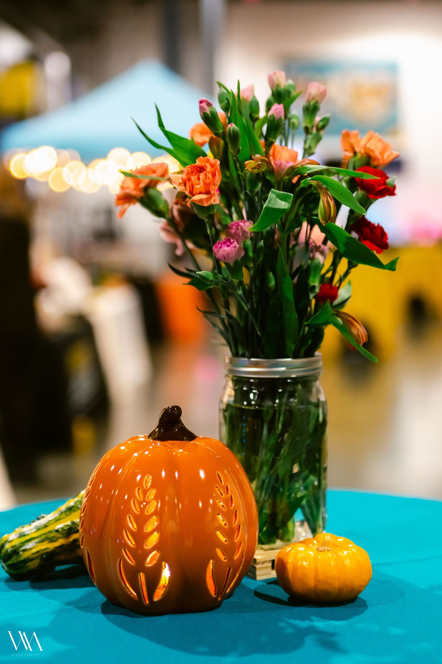 Ceramic pumpkin and mason jar with orange flowers on a teal table at a fall harvest event.