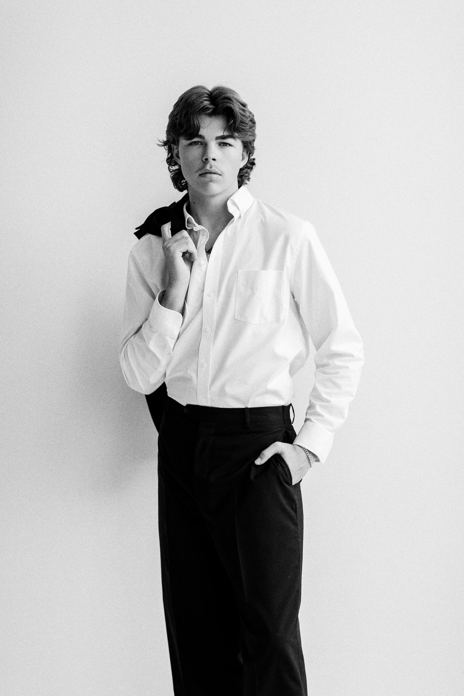 Black and white portrait of a young man in white shirt and black trousers, posing confidently against a light background.