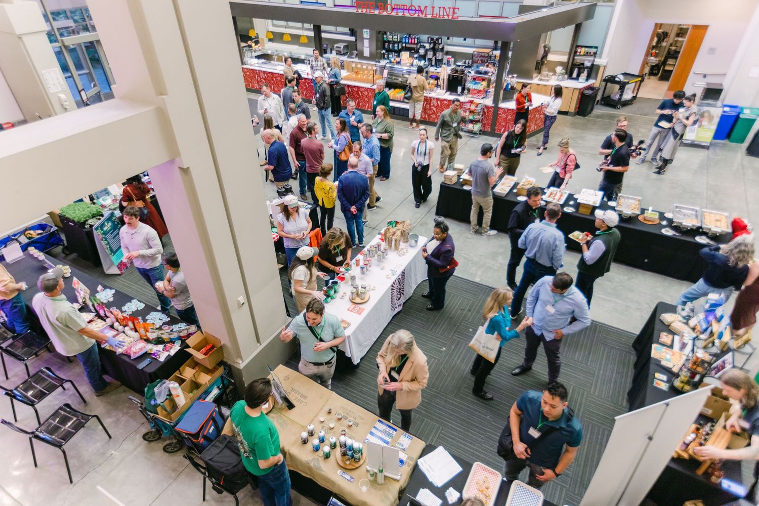 Overhead view of busy indoor market with vendors and shoppers browsing tables of goods.