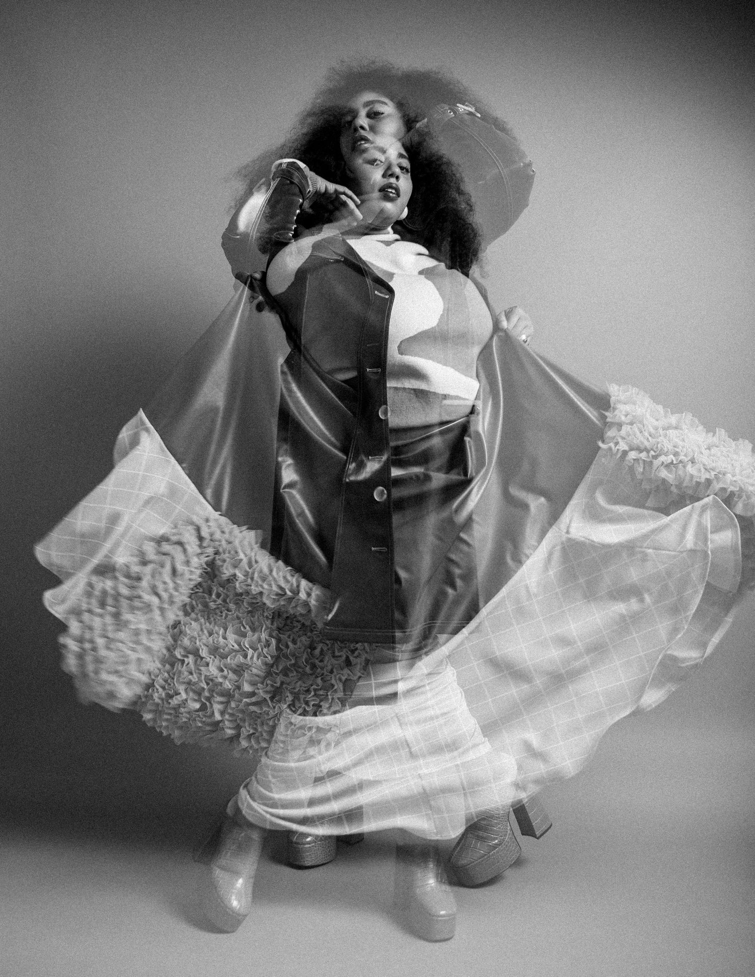 Black and white photo of a woman dancing in flowing sheer fabric and layered outfit, captured mid-movement in studio.
