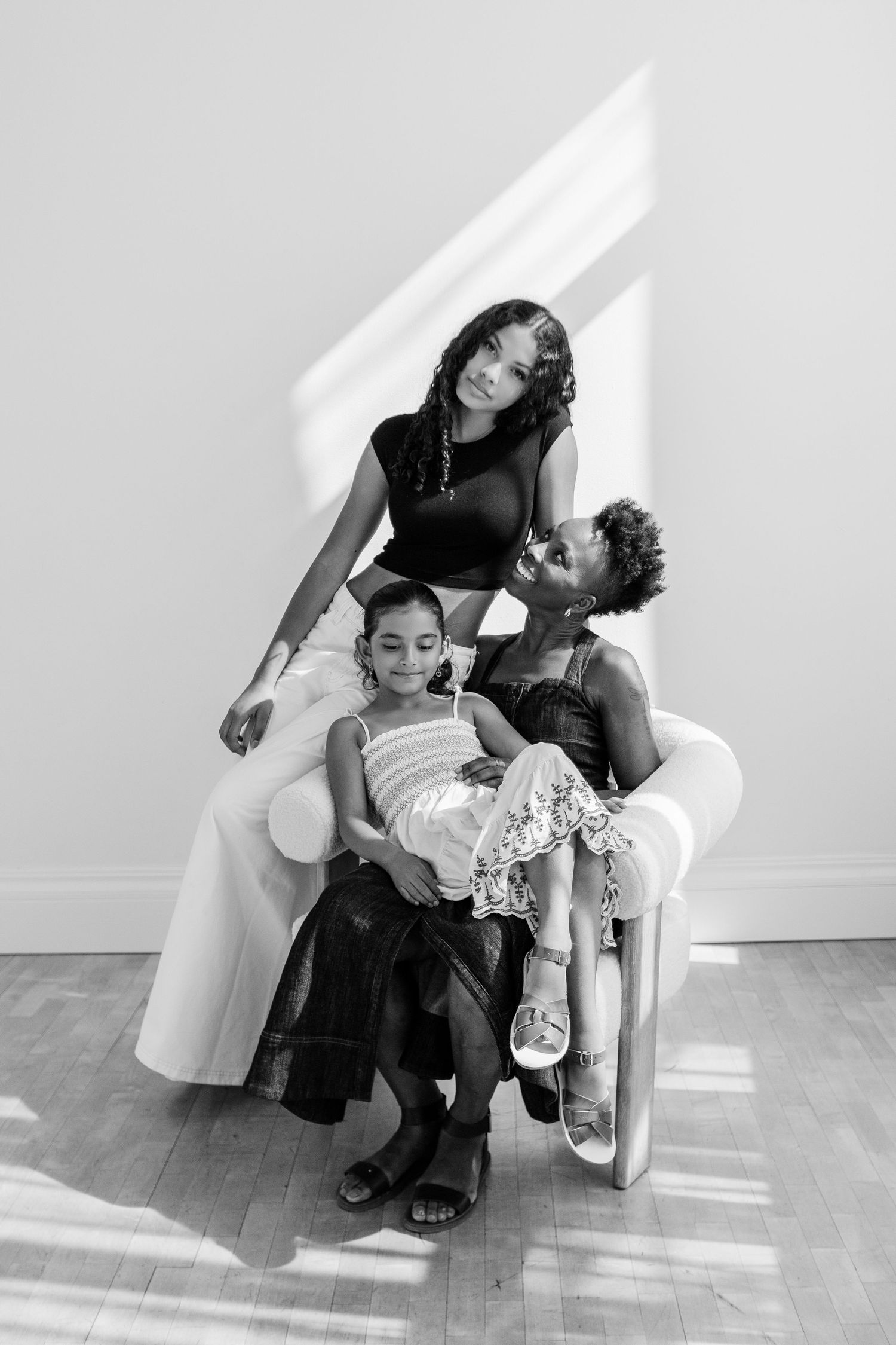 A black and white portrait of two women and a young girl posing together in a white chair.