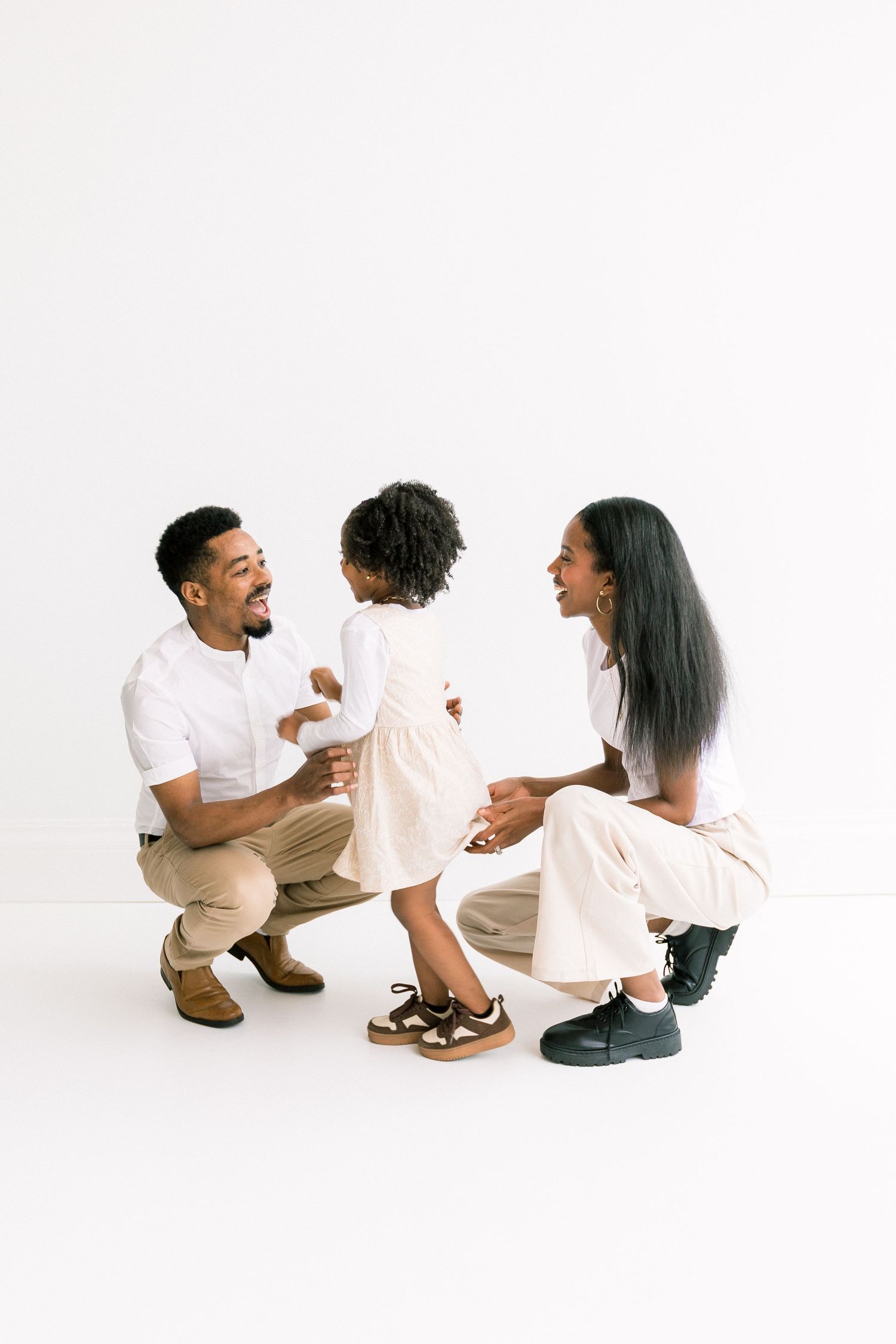 Loving parents crouching down smiling at their young daughter in a white studio.